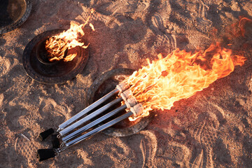 Top view of burning fire torches on sand as equipment for outdoor fire show in nature, copy space