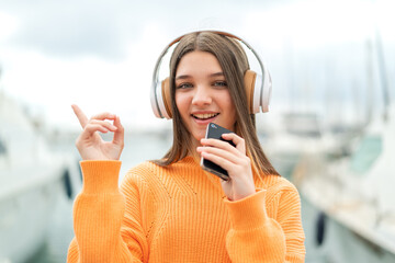 Teenager girl at outdoors listening music with a mobile and singing