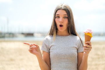Teenager girl with a cornet ice cream at outdoors surprised and pointing side