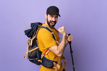 Caucasian handsome man with backpack and trekking poles over isolated background celebrating a...