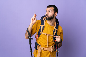Caucasian handsome man with backpack and trekking poles over isolated background with fingers crossing and wishing the best