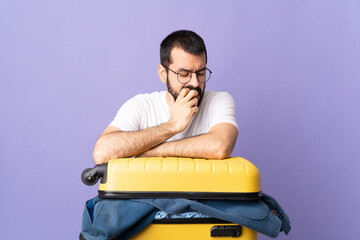 Traveler caucasian man with a suitcase full of clothes over isolated purple background having doubts