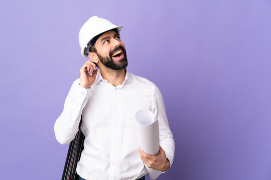 Young architect man with helmet and holding blueprints over isolated purple background thinking an idea