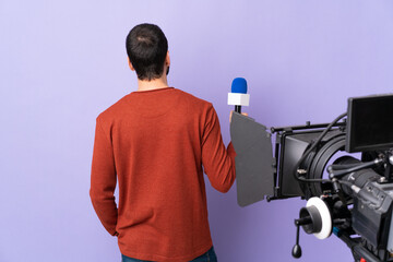 Reporter man holding a microphone and reporting news over isolated purple background in back position