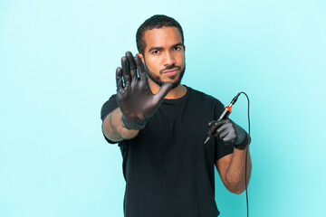 Tattoo artist Ecuadorian man isolated on blue background making stop gesture