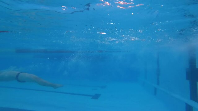 View from the depths of the pool. A young swimmer makes a turn underwater. Professional swimming athlete in a large sports pool.