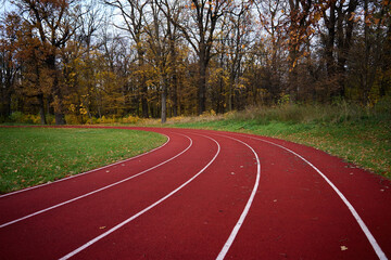 Obraz premium Red runninng race track with lanes at autumn park, Treadmill at stadium, Sport and fitness concept