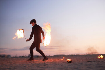 Full length side view of male fire show performer dancing with flames in nature during sunset, copy...
