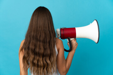 Young hispanic woman over isolated blue background holding a megaphone and in back position