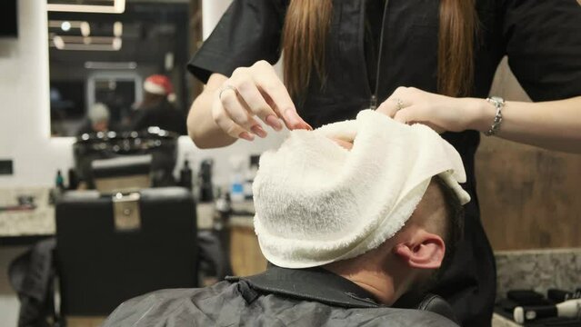 A barber grooms a client's beard using cosmetic trimming tools and professional grooming. Brutal dark interior. Professional hairdresser-stylist working with a client.