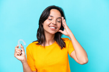 Young hispanic woman holding invisible braces isolated on blue background smiling a lot