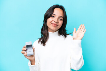 Young hispanic woman holding a engagement ring isolated on blue background saluting with hand with...