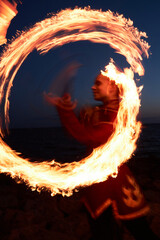 Blurred motion shot of young woman spinning fire circle outdoors at night during fire show © Seventyfour