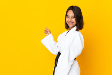 Young woman doing karate isolated on yellow background pointing back