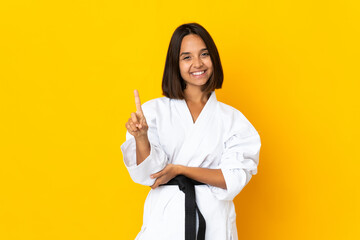 Young woman doing karate isolated on yellow background showing and lifting a finger