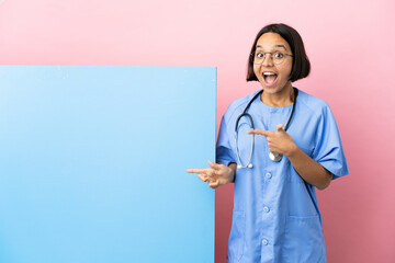 Young mixed race surgeon woman with a big banner over isolated background surprised and pointing...