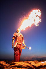 Full length portrait of young man breathing fire performing outdoors at night