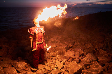 High angle portrait of young man breathing fire performing on beach outdoors, copy space