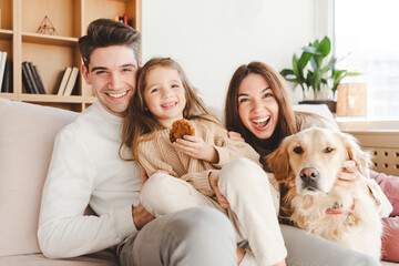Happy attractive young family hugging at cozy home. Portrait smiling father, mother, cute little...