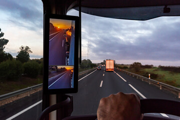 View from the driver's position of a truck on the road of a sunrise seen by the vehicle's rearview...