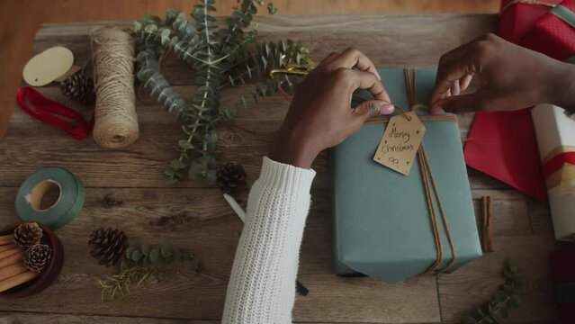 Directly above view of female hands tying twine while making gift with postcard Merry Christmas