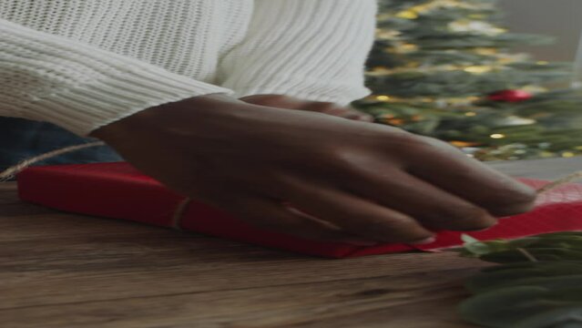 Vertical shot of person decorating Christmas gift using twine wrapping with red paper while crafting on table