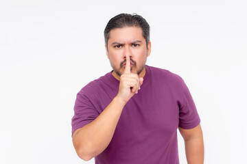 An angry man tells someone to shut up and keep quiet. Hush gesture with finger. Wearing a purple shirt, isolated on a white background.