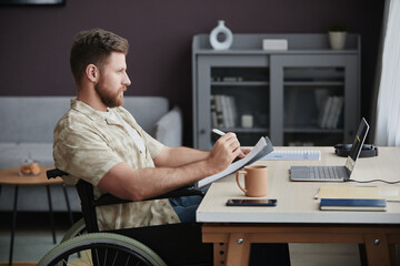 Side view portrait of bearded man with disability designing mobile app while working at home office and holding plans