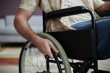Close up of unrecognizable person with disability turning wheelchair wheel in home setting, copy space