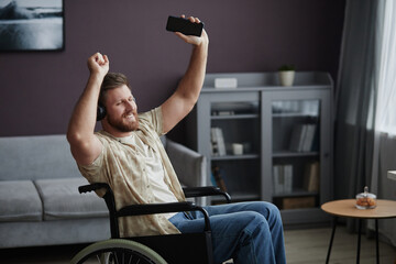 Portrait of bearded man with disability dancing in wheelchair at home and listening to music, copy space