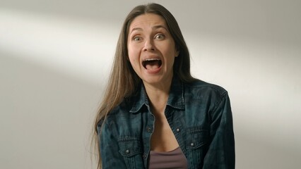 Portrait of appealing female model in friendly mood. Brunette woman in casual on white background in the studio wide open eyes laughing.