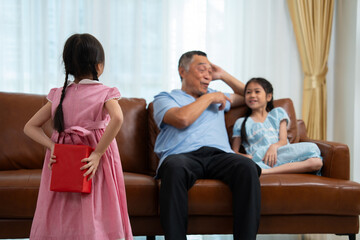 Little girl hiding present box behind back while making surprise elderly grandparents, Cheerful...