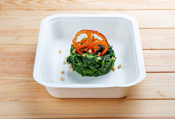 Braised spinach with pine nuts. Healthy food. Takeaway food.  On a wooden background.
