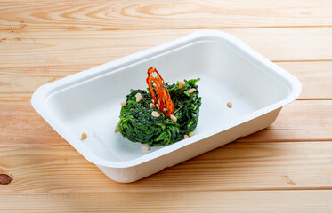Braised spinach with pine nuts. Healthy food. Takeaway food.  On a wooden background.