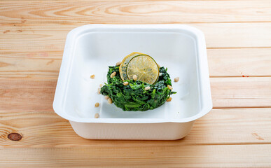 Braised spinach with pine nuts. Healthy food. Takeaway food.  On a wooden background.