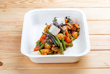 Sautéed vegetables. Healthy diet. Takeaway food. Ecological packaging. On a wooden background.