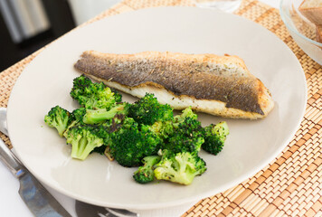 Fried fillet of sea bass with garnish of broccoli on black warm stone plate