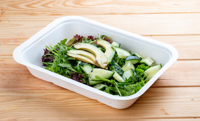 Salad with greens and avocado. Vegetarian food. Takeaway food. On a wooden background.