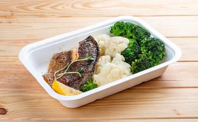 Sea bass fillet, blanched broccoli and cauliflower. Healthly food. Takeaway food. On a wooden...