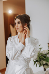 A beautiful brunette bride with a tiara in her hair is getting ready for the wedding in a beautiful robe in boudoir style. Close-up wedding portrait, photo.