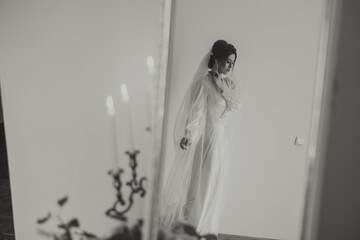 portrait of a luxurious bride in boudoir style near a mirror with reflection. Preparing the bride for the wedding in the morning in a white robe.