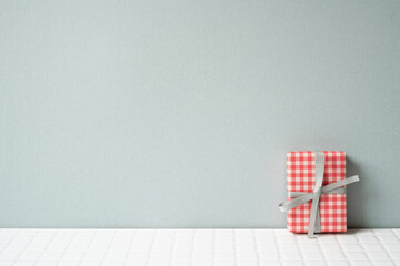 Red check pattern gift box on white tile table. gray wall background. copy space