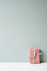 Fototapeta na wymiar Red check pattern gift box on white tile table. gray wall background. copy space