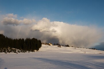 Big clouds over a village house on a hill on a winter evening