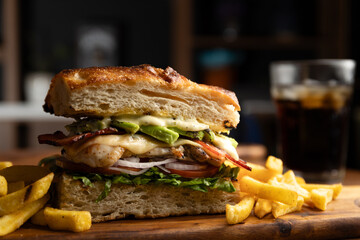 Grilled chicken breast sandwich with lettuce, tomato, bacon, red onion rings and avocado served on artisan bread and a portion of French fries