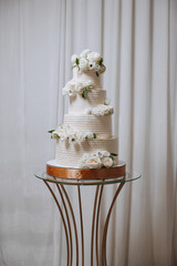 A large luxurious multi-tiered wedding cake is decorated with fresh white rose flowers in the banquet hall. Wedding dessert under the evening light. Wedding decor.