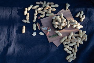 Top down view on a peanuts in a shell laying in a group on a blue fabric table cloth. Some peanuts are peeled.