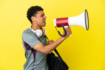 Young sport African American man with sport bag isolated on yellow background shouting through a...