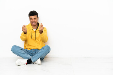 Young African American man sitting on the floor isolated on white background making money gesture