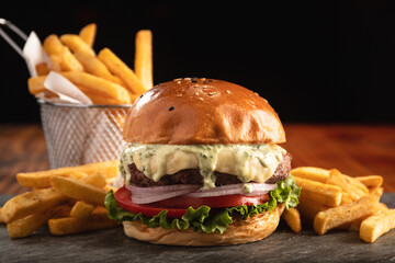 Burger with cheese, tomato, lettuce, bacon and red onion rings, with aioli sauce and a portion of...